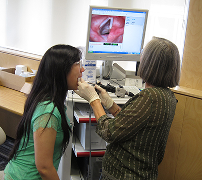 Research Associate Linda Rammage demonstrates  on student Clara Liu how speech-language pathologists use laryngoscopy to examine a person's vocal cords.