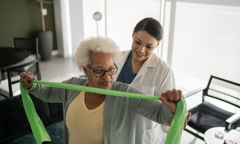 A physician helps an elderly patient perform exercises with a resistance band. 