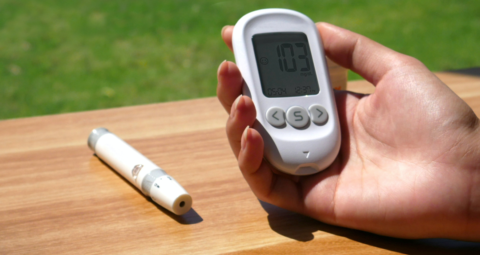 A person holding a digital thermometer next to a pen