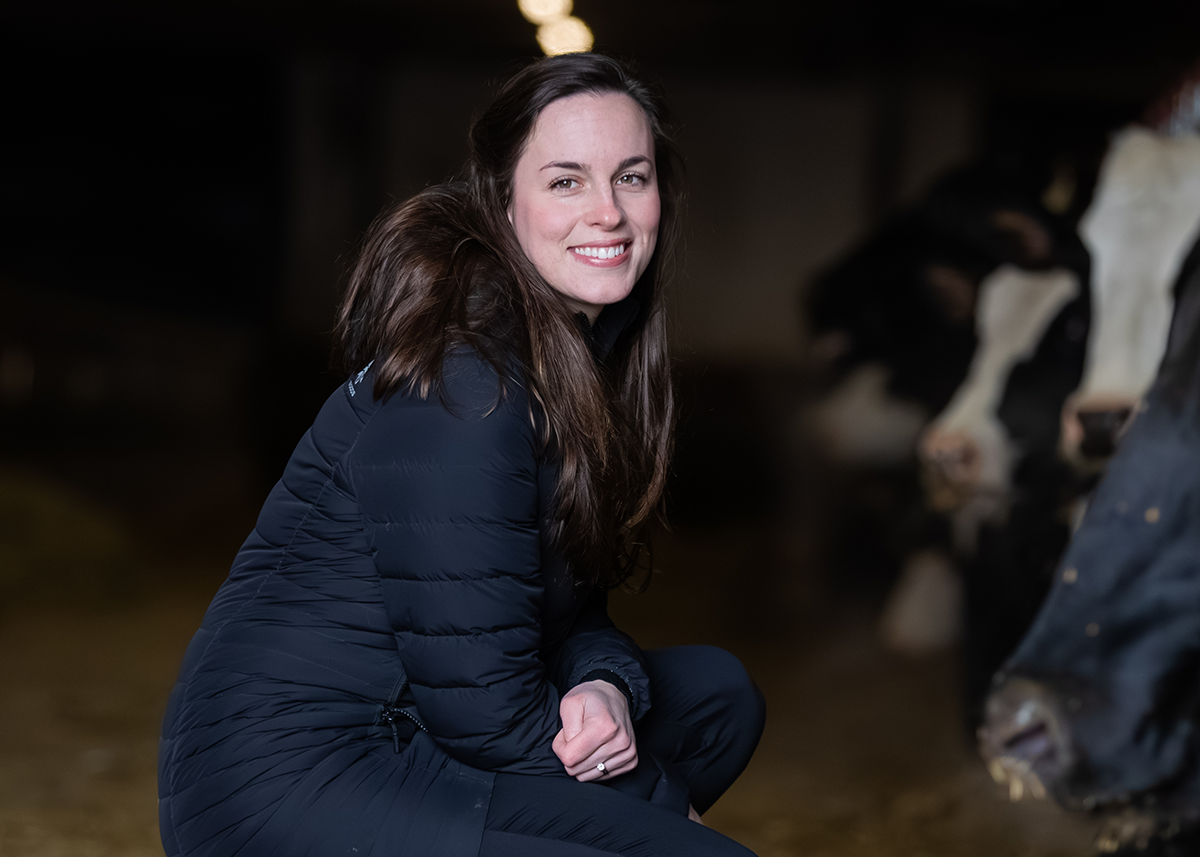 A picture of Dr. Jenn Vandenburg posing in front of the cows in her dairy farm